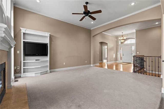 unfurnished living room with crown molding, ceiling fan with notable chandelier, a tile fireplace, and carpet