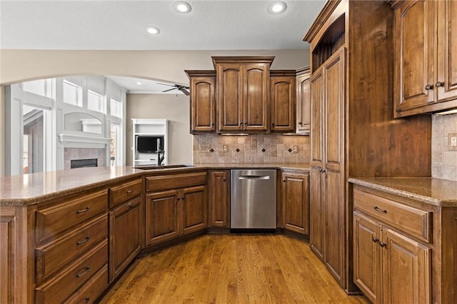 kitchen with a tile fireplace, ceiling fan, backsplash, light stone countertops, and light hardwood / wood-style floors