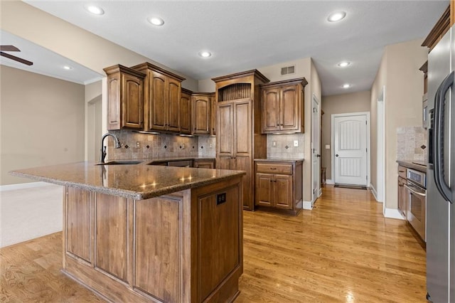 kitchen with sink, dark stone countertops, oven, and light wood-type flooring