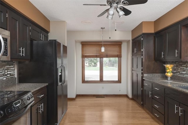 kitchen with dark stone countertops, backsplash, hanging light fixtures, black appliances, and light hardwood / wood-style flooring