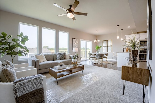 living area with light wood-type flooring, baseboards, and ceiling fan with notable chandelier