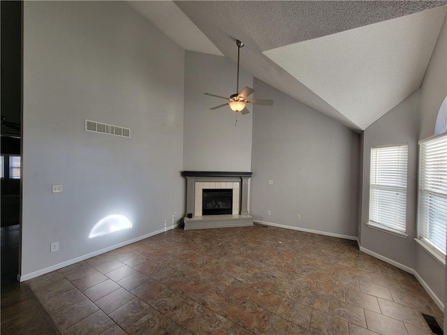 unfurnished living room with ceiling fan, a textured ceiling, high vaulted ceiling, and a tiled fireplace