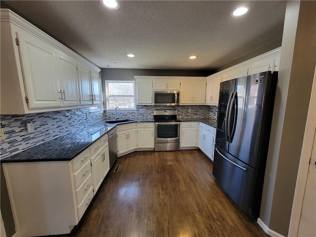 kitchen with appliances with stainless steel finishes, a textured ceiling, dark wood-type flooring, sink, and white cabinets