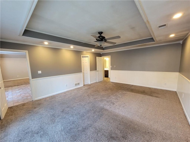 carpeted empty room with a raised ceiling, ceiling fan, and ornamental molding