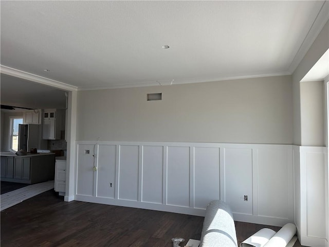 interior space featuring dark wood-style floors, a decorative wall, wainscoting, and crown molding