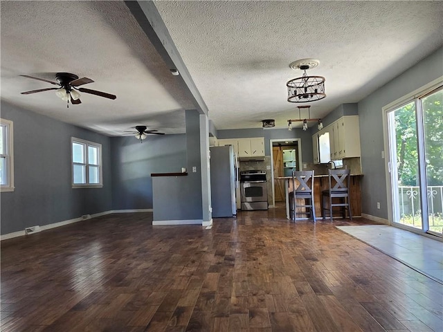 unfurnished living room with dark wood-type flooring, ceiling fan with notable chandelier, and a textured ceiling