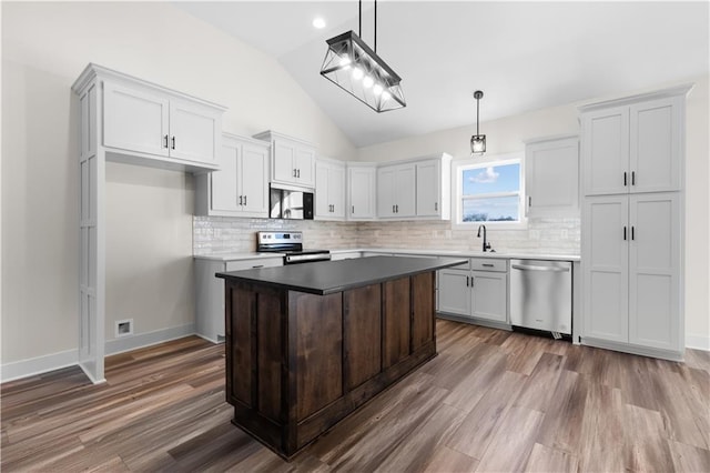 kitchen featuring decorative light fixtures, vaulted ceiling, a center island, appliances with stainless steel finishes, and dark wood-type flooring