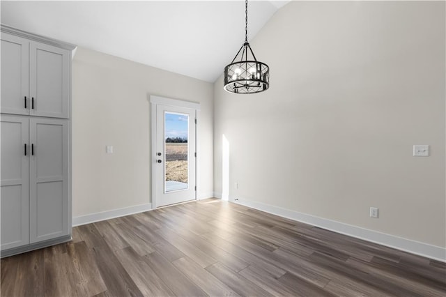 unfurnished dining area with dark hardwood / wood-style floors, lofted ceiling, and an inviting chandelier