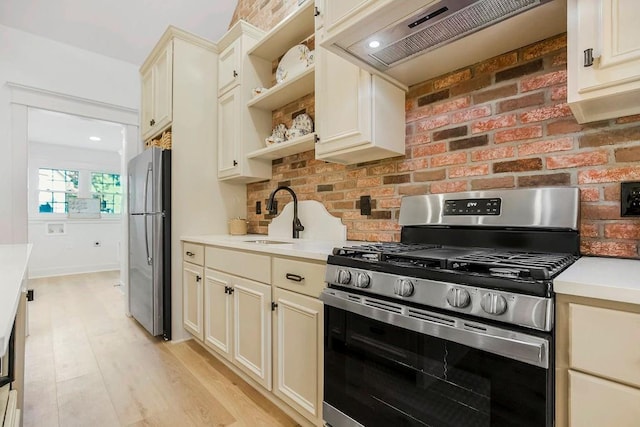 kitchen featuring premium range hood, appliances with stainless steel finishes, sink, light hardwood / wood-style floors, and cream cabinetry