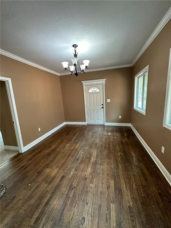 spare room featuring crown molding, a textured ceiling, a chandelier, and dark hardwood / wood-style floors