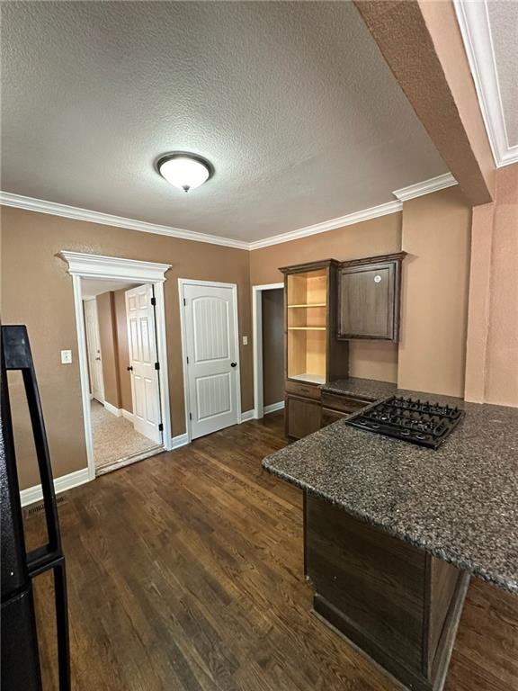 kitchen featuring dark stone countertops, crown molding, a textured ceiling, dark wood-type flooring, and black gas stovetop