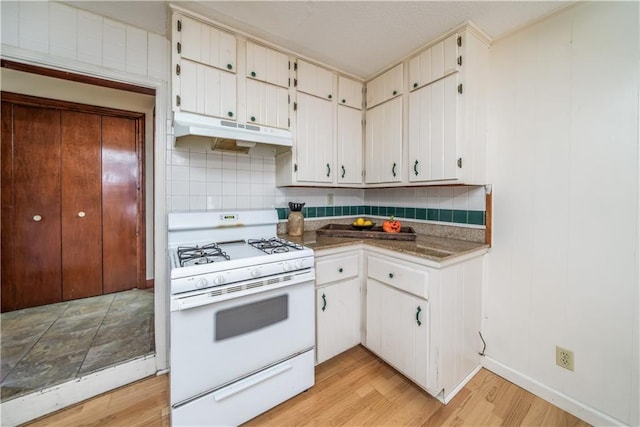 kitchen with backsplash, white gas stove, light hardwood / wood-style flooring, and white cabinets