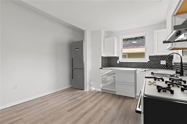 kitchen featuring stainless steel fridge, white stove, light hardwood / wood-style flooring, decorative backsplash, and white cabinets