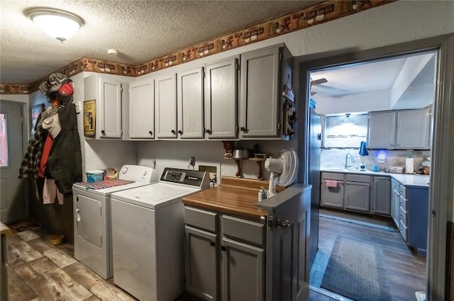 clothes washing area featuring sink, a textured ceiling, cabinets, hardwood / wood-style flooring, and washing machine and dryer