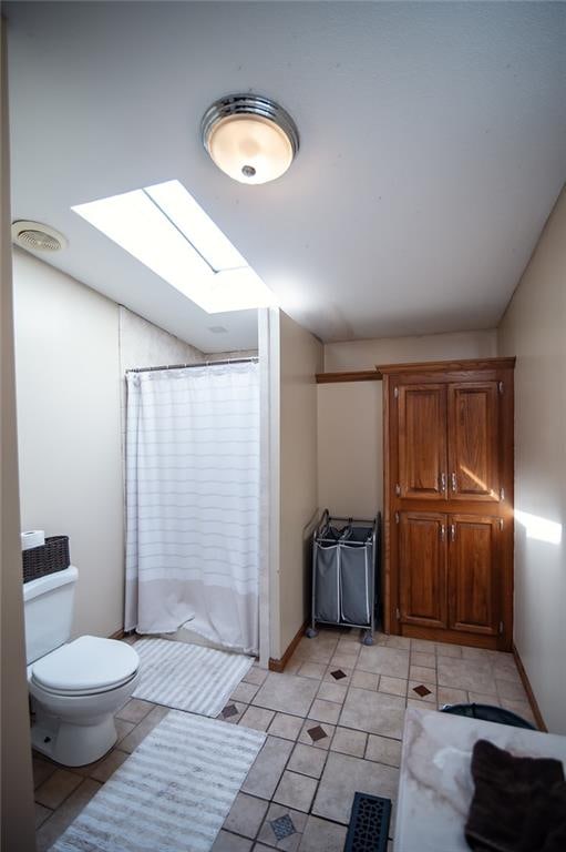 bathroom featuring a skylight, tile patterned floors, toilet, and curtained shower