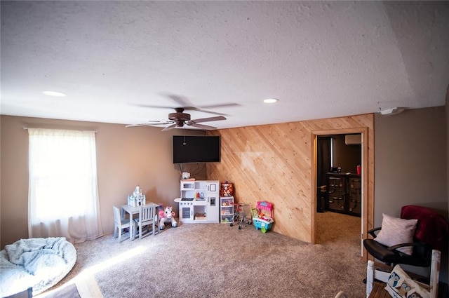 recreation room with ceiling fan, wood walls, carpet flooring, and a wall unit AC