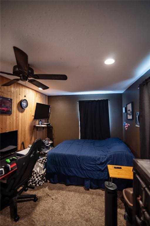 bedroom with ceiling fan, wood walls, and carpet