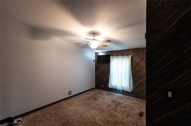 spare room featuring wood walls, carpet flooring, a textured ceiling, and ceiling fan