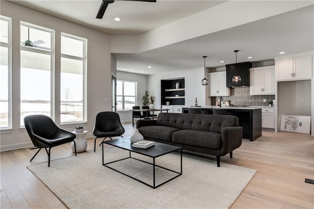 living room with ceiling fan, sink, light hardwood / wood-style flooring, and built in features