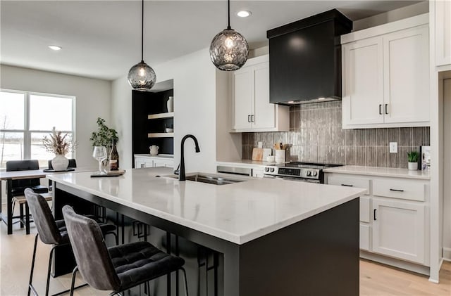 kitchen with white cabinetry, sink, a kitchen island with sink, and wall chimney exhaust hood