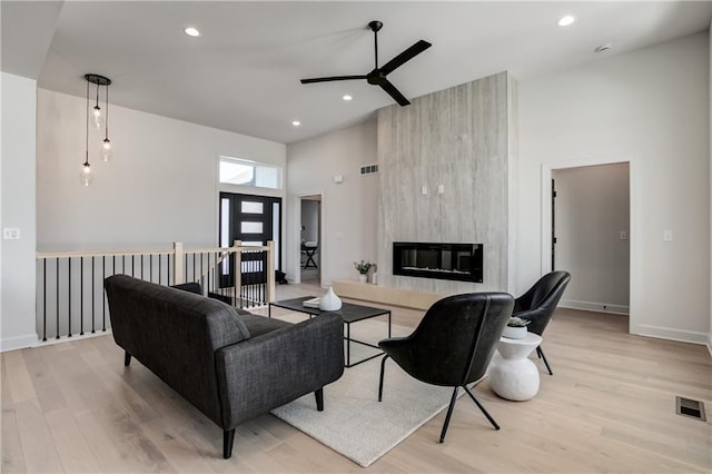 living room featuring ceiling fan, a large fireplace, a high ceiling, and light wood-type flooring