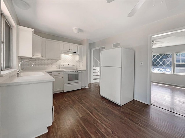 kitchen featuring visible vents, a sink, under cabinet range hood, white appliances, and dark wood-style flooring