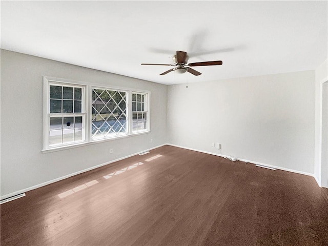 empty room with dark wood-type flooring, visible vents, baseboards, and ceiling fan