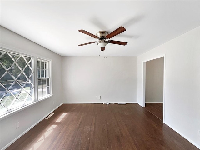 empty room with a ceiling fan, wood finished floors, visible vents, and baseboards