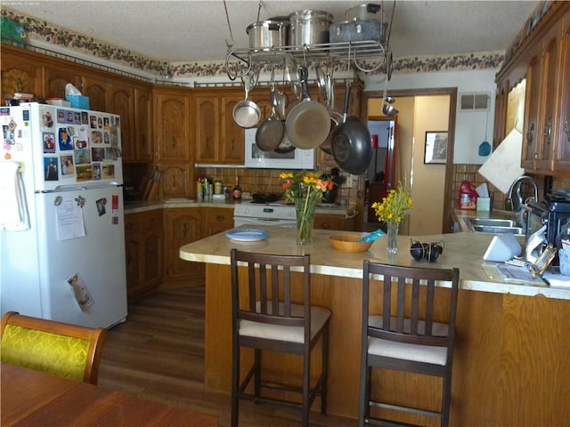 kitchen featuring white appliances, kitchen peninsula, sink, dark wood-type flooring, and a breakfast bar area