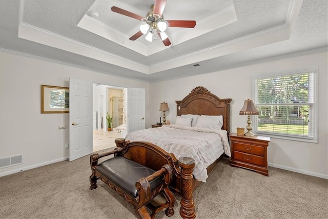 bedroom featuring a raised ceiling, light carpet, crown molding, ensuite bath, and ceiling fan