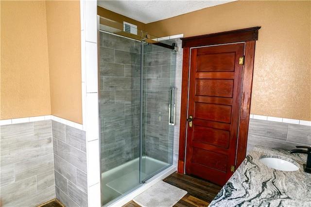 bathroom with a textured ceiling, a shower with shower door, vanity, hardwood / wood-style floors, and tile walls