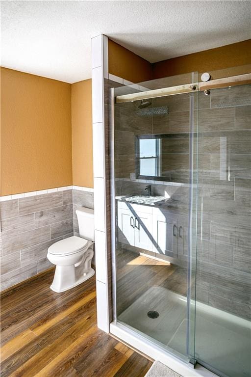 bathroom featuring a textured ceiling, wood-type flooring, walk in shower, tile walls, and toilet