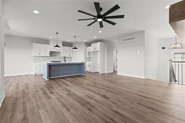 unfurnished living room with hardwood / wood-style floors, ceiling fan with notable chandelier, and sink