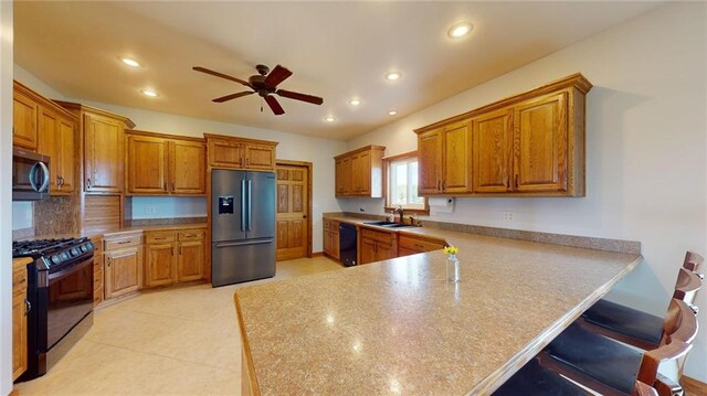 kitchen featuring kitchen peninsula, black appliances, a kitchen bar, ceiling fan, and sink