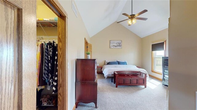 bedroom with ceiling fan, high vaulted ceiling, a walk in closet, a closet, and light colored carpet