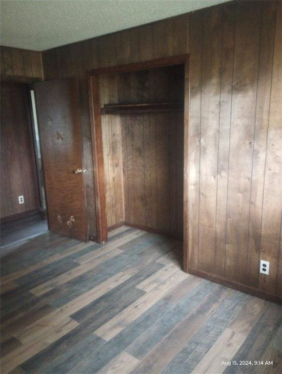 unfurnished bedroom with a textured ceiling, a closet, wood-type flooring, and wooden walls