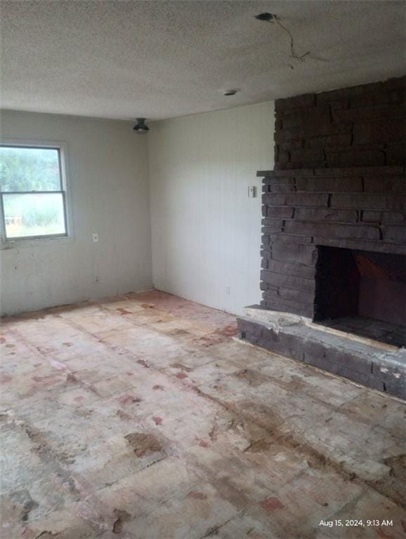 unfurnished room with a textured ceiling and a brick fireplace