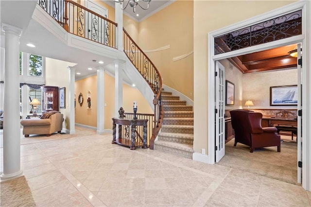 staircase featuring tile patterned flooring, a towering ceiling, ornamental molding, and decorative columns