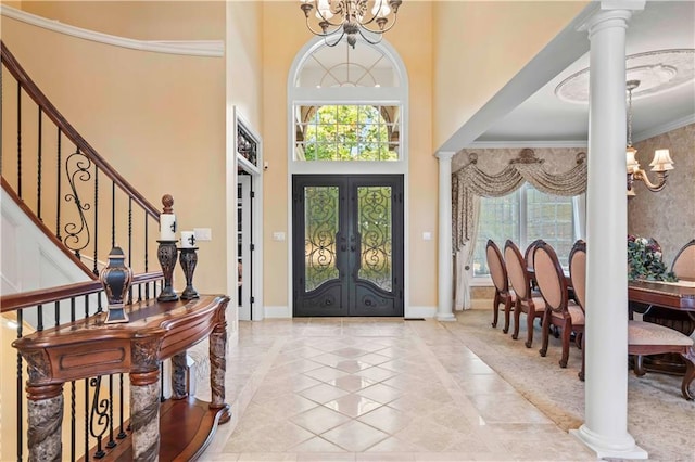 foyer entrance with crown molding, decorative columns, an inviting chandelier, a towering ceiling, and french doors