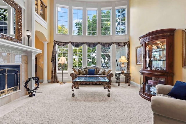 living room with a healthy amount of sunlight, a tiled fireplace, carpet floors, and a towering ceiling