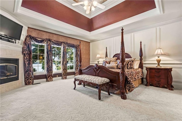 bedroom featuring a tiled fireplace, a raised ceiling, and crown molding