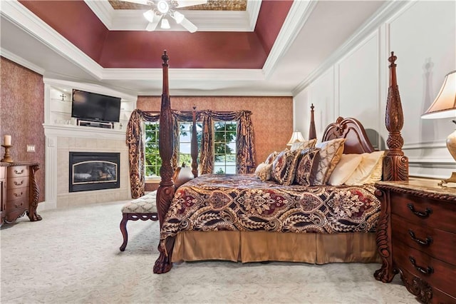 bedroom with crown molding, ceiling fan, a tile fireplace, and a tray ceiling