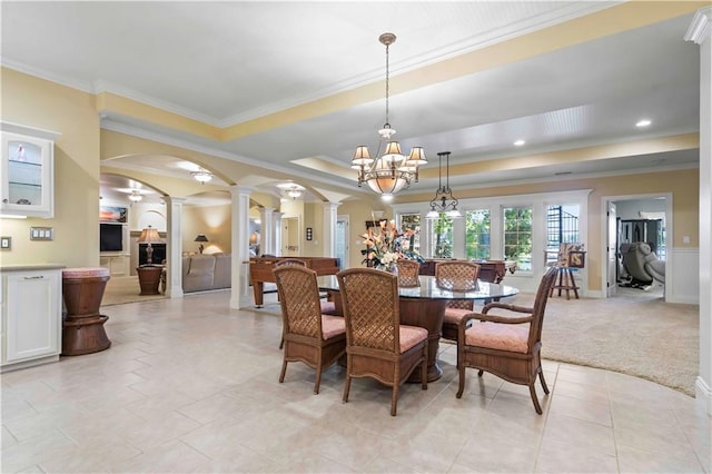 dining room with light colored carpet, a chandelier, ornate columns, a tray ceiling, and ornamental molding