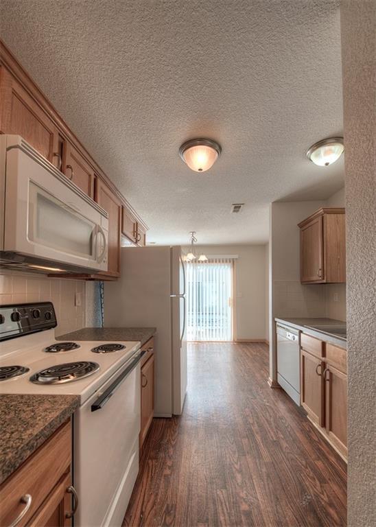 kitchen featuring a textured ceiling, decorative light fixtures, white appliances, backsplash, and dark wood-type flooring