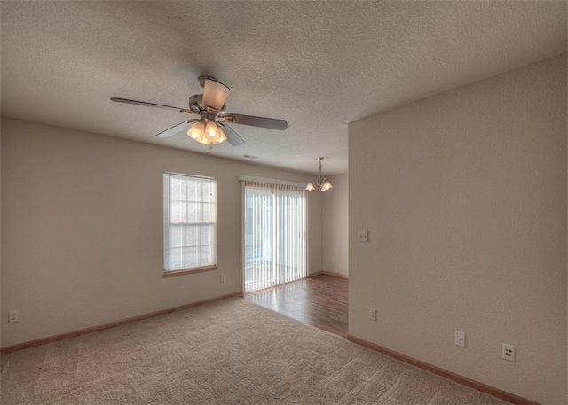 carpeted empty room featuring ceiling fan with notable chandelier and a textured ceiling