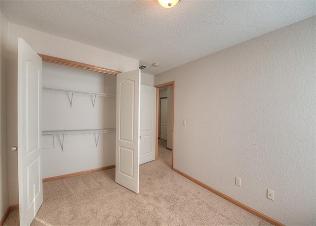 unfurnished bedroom featuring a textured ceiling, light colored carpet, and a closet