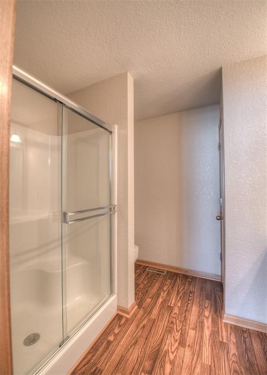 bathroom with an enclosed shower, hardwood / wood-style floors, toilet, and a textured ceiling