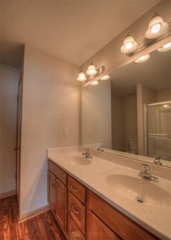 bathroom with a textured ceiling, vanity, an enclosed shower, hardwood / wood-style floors, and toilet