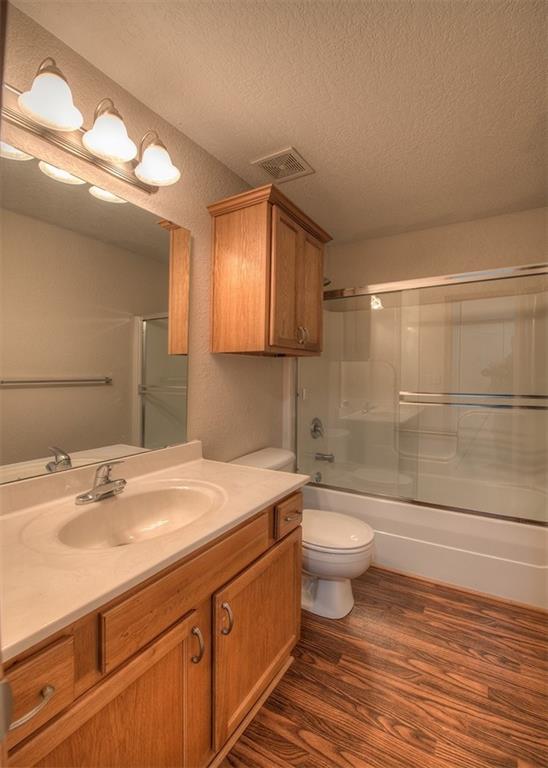 full bathroom with hardwood / wood-style flooring, toilet, combined bath / shower with glass door, vanity, and a textured ceiling