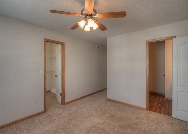 unfurnished bedroom featuring light colored carpet, a walk in closet, a closet, ceiling fan, and a textured ceiling